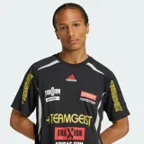 Camiseta de manga corta Adidas Teamgeist de color negro, con cuello redondo y diseño gráfico con estampas y patrocinadores deportivos en el pecho y las mangas. Presenta detalles en blanco y gris en los laterales.