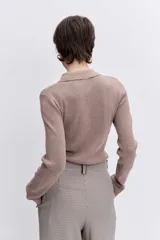 Jersey de punto color beige con cuello polo y cierre frontal de botones. Presenta mangas largas y un ajuste entallado al cuerpo.