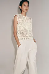 Blusa sin mangas confeccionada en tejido tipo crochet con diseño geométrico calado, cuello redondo y cierre frontal con botones.