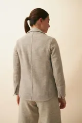 Chaqueta marrón de lana con cuello, solapa y bolsillos ojal. Forro solo en las mangas y terminaciones envivadas. Esquinas redondeadas y mangas con corte en puño que permiten transformarla en manga 3/4. Más larga en la espalda que en la delantera. Abrochadura con dos botones.