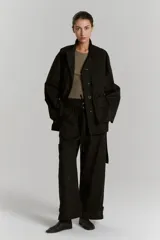 Parka negra de gabardina con corte amplio, cuello camisero, manga amplia con recortes y presillas en puños, cartera de botones oculta, bolsillos plaque con tapa, canesú con pestaña en delantero y cinturón con medialuna metálica.