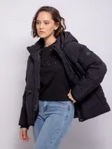 Campera puffer negra de nylon con capucha, cierre frontal, tres bolsillos y elástico regulable en cintura y puños.