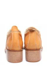 Zapato de cuero color ocre, con elásticos laterales, taco bajo y puntera fina con diseño bordado.