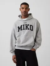 Canguro gris con capucha, diseño holgado y bolsillo frontal tipo canguro. Presenta estampado frontal con la palabra 'MIKO' en letras negras y bordado de la marca en el puño.