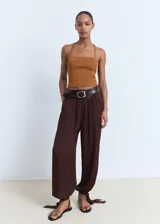 Pantalón estilo globo de color marrón, con diseño abullonado en el bajo, cintura elástica y detalle de lazos ajustables en los tobillos.