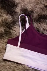 Top deportivo de entrenamiento con doble capa, color blanco exterior y borgoña interior. Presenta un corte de tirantes anchos y el logo "Hermod" en cursiva color borgoña en el pecho.