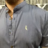 Camisa de hombre azul marino con rayas verticales finas blancas, cuello mao, cierre con botones marrones y logo bordado en el pecho.