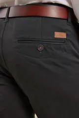 Pantalón de vestir verde oliva, de corte slim fit, sin pinzas, con bolsillos laterales y traseros. Se ajusta a la cintura con cinturón de cuero marrón.