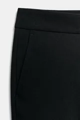 Pantalón de tiro alto color beige, de corte recto y largo tobillero, con bolsillos laterales y cierre frontal con cremallera y ganchos metálicos.