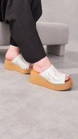 Zuecos con plataforma corrida de yute y suela de goma, capellada ancha de color marfil con textura símil serpiente y diseño abierto en la punta.