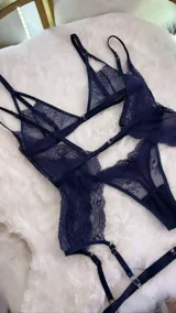 Set de lencería de cuatro piezas en encaje azul marino. Incluye bralette con breteles regulables y broche frontal, tanga colaless regulable con entrepierna de algodón, y chaleco con portaligas integrado con ligas regulables.