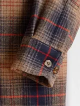 Camisa de lana a cuadros color marrón, azul y rojo, de corte recto con cuello camisero, cierre frontal con botones, dos bolsillos con solapa abotonados en el pecho y mangas largas con puños abotonados.
