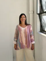 Sweater de punto con diseño abstracto en tonos rosados, beige y azul, de corte holgado, cuello en V y mangas largas con puños vueltos.