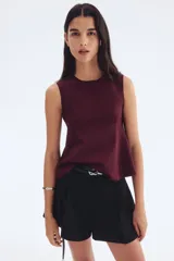 Musculosa sin mangas color vino tinto, con cuello redondo y corte peplum que se ajusta en el torso y se abre ligeramente en el ruedo. Presenta paneles laterales curvos que moldean la figura.