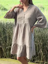 Vestido corto de lino color beige claro, con cuello mao, escote con botones de nácar, mangas tres cuartos con volados y ruedo con volado.