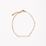 Pulsera dorada con cadena de eslabones y dije de barra horizontal con incrustaciones de circonitas.