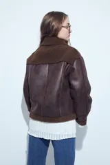 Gamulán de cuero sintético en color marrón oscuro con interior de corderito al tono. Presenta cierre diagonal, cuello amplio con solapas y puños con detalle de corderito.