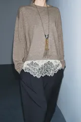Jersey de punto color beige con cuello redondo y manga larga. Presenta un diseño de bajo combinado con un detalle de encaje en color crema.