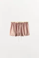Shorts de tiro bajo en mezcla de viscosa y lino, color rosado con sutiles rayas verticales. Presenta cintura elástica fruncida con lazada frontal ajustable y aplicación de puntilla en contraste en el borde superior. Diseño de bajo abullonado tipo globo.