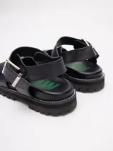 Sandalias romanas de cuero tostado, estilo chunky con plataforma y suela tractora de goma negra. Cuentan con tiras cruzadas en el empeine y tira ajustable con hebilla metálica en el tobillo.
