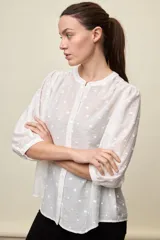 Camisa negra de textura liviana con detalle de lunares en relieve, cuello mao y cierre frontal con botones. Presenta mangas 3/4 con puños elastizados y frunces en los hombros.