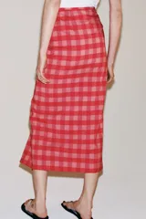 Falda midi de tiro medio, con estampado a cuadros vichy en tonos rojo y rosado, detalle de volantes en el delantero y cierre lateral con cremallera oculta.