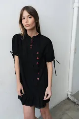 Vestido corto negro de broderie con cartera de botones asimétrica, mangas cortas abullonadas con lazo y volado en el ruedo.