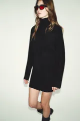 Vestido corto de punto con cuello subido, manga larga y sisa ancha. Presenta un detalle de costura vertical marcada en el centro del delantero y acabados en rib en cuello, puños y ruedo.