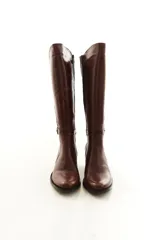 Bota de caña alta confeccionada en cuero legítimo color marrón, con diseño clásico, costuras visibles y una delicada tira con hebilla lateral. Cuenta con cierre lateral interno y taco medio ancho.