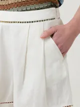 Short de tiro medio confeccionado en mezcla de lino orgánico y viscosa, color beige. Presenta diseño con pinzas frontales, bolsillos laterales y detalles de calados decorativos en la cintura y en el ruedo.