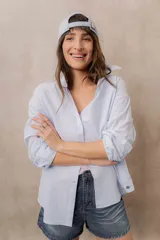 Camisa blanca de calce amplio, confeccionada en tejido liviano con sutiles rayas verticales, cuello clásico, mangas largas con hombros caídos y abotonadura frontal.