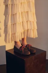 Mocasín tipo boat shoe color marrón, confeccionado en cuero, con cordones de cuero marrón y cordones decorativos azules.