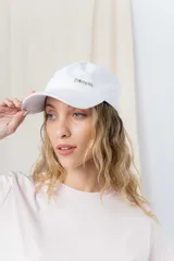 Gorra verde militar de diseño clásico con visera curva y aplique metálico plateado con la inscripción "Peach" en el lateral frontal. Cuenta con tira ajustable en la parte trasera.