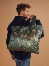 Bolso tote reutilizable de tela Tyvek con estampado abstracto en tonos verdes y negros. Asas de cinta gross negra con inscripción "THOMAS".