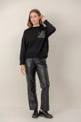 Sweater negro de punto con cuello redondo, mangas largas y un bolsillo frontal decorado con lentejuelas brillantes.
