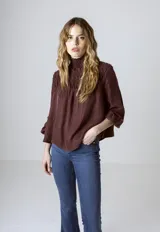 Blusa de cuello alto fruncido y diseño holgado, con mangas largas abullonadas y detalle de nido de abeja en el canesú delantero y posterior.