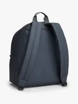 Mochila de diseño redondeado en color gris, con compartimento principal amplio, bolsillo frontal con cierre y parche distintivo de la marca en la parte inferior. Cuenta con asa superior y correas acolchadas ajustables.