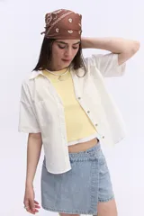 Camisa de manga corta color rosado, con cuello camisero, cierre frontal con botones y dos bolsillos delanteros con solapa. Presenta un corte corto y holgado, con dobladillo redondeado.