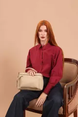 Bandolera de diseño rectangular en color suela, confeccionada en material sintético. Cuenta con un asa superior fija, correa larga ajustable y extraíble, y dos bolsillos frontales con cierre metálico, uno de ellos con diseño superpuesto. Presenta el logo de la marca grabado en el frente.