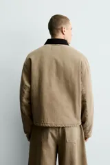 Cazadora de corte relajado confeccionada en algodón con efecto lavado. Presenta cuello de solapa en contraste de color negro, cierre frontal con cremallera oculta y alamares metálicos, bolsillos laterales de vivo y mangas largas.