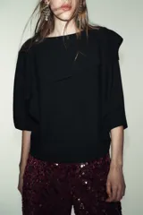 Jersey negro de punto con cuello asimétrico, manga ancha y diseño de capa superpuesta.