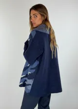 Saco de lana color verde militar con estampado abstracto en tonos verde oliva y detalles bordados en rojo. Tiene cuello solapa, cierre frontal con botones de madera y puños acanalados.