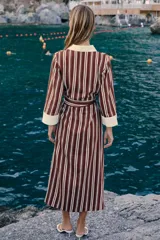 Vestido midi camisero de rayas verticales en tonos bordó y blanco, con cuello solapa y puños en color contrastante. Cuenta con mangas largas, cierre frontal de botones y un cinturón ajustable con hebilla metálica en la cintura.