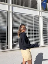 Buzo de punto color negro con cuello polo abierto, mangas largas amplias y corte cropped de silueta relajada.