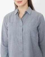 Camisa celeste de manga larga con cuello clásico, cierre con botones y dos bolsillos en el pecho.