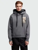 Buzo con capucha gris de Moncler, con cordones negros y parche bordado en el pecho con diseño de paisaje montañoso y logo de la marca.