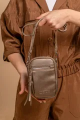 Bandolera compacta color rosado, con correa regulable y desmontable. Tiene apertura superior, bolsillo frontal con cierre y detalle de borla, y bolsillo trasero sin cierre. El interior está forrado en tela y cuenta con un bolsillo adicional.