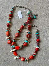 Collar artesanal compuesto por una mezcla de cuentas de coral rojo, piedras turquesas, piezas de nácar y pequeñas cuentas metálicas. Presenta una cadena de acero con cierre de mosquetón.