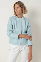 Campera de cuero ovino color celeste claro, estilo chaqueta corta, con cuello redondo y cierre frontal de botones. Presenta bolsillos delanteros con solapa curva.