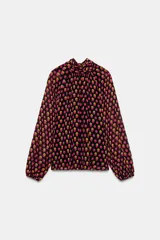 Camisa de cuello subido y manga larga con puños elásticos. Presenta un diseño de lunares en tonos fucsia y amarillo sobre fondo negro, con detalle de pliegues en el frente y cierre de cremallera oculta en la espalda.